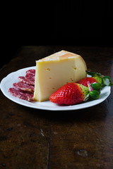 Fontina, salame e fragole su piatto tavolo e sfondo nero
