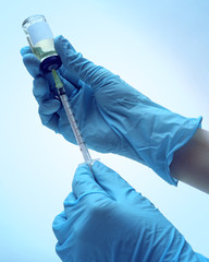 Hands in gloves filling medicine from ampule into syringe