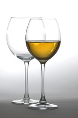 Two tall glasses, empty and filled with white wine