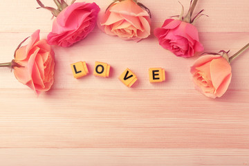Beautiful roses with word LOVE on wooden background