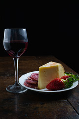 Piatto Fontina, salame, fragole e vino rosso sfondo nero