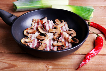 Strips of bacon with mushrooms in pan, chili pepper and shallot