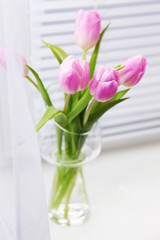 Beautiful pink tulips in glass vase on windowsill background
