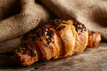 Fresh and tasty croissant with chocolate on wooden background