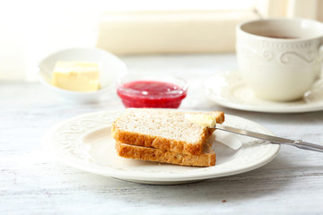 Toasts with butter on plate with cup of tea on light background