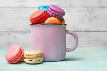Tasty colorful macaroons in mug on color wooden background