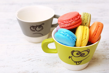 Tasty colorful macaroons and cups on color wooden background