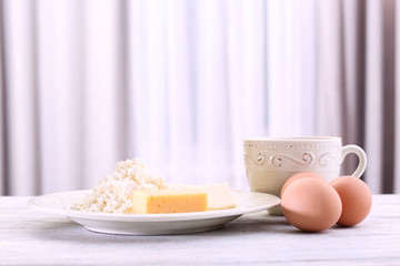 Eggs and dairy products on wooden table on curtain background