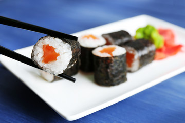 Sushi rolls with salmon on plate, on wooden background