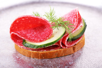 Sandwich with salami and cucumber on metal tray background