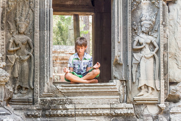 young happy child boy tourist meditating in angkor wat, cambodia