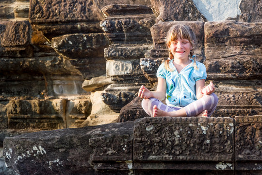 young happy child girl tourist meditating in angkor wat, cambodi
