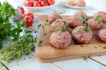 Raw meat balls with herbs on wooden board