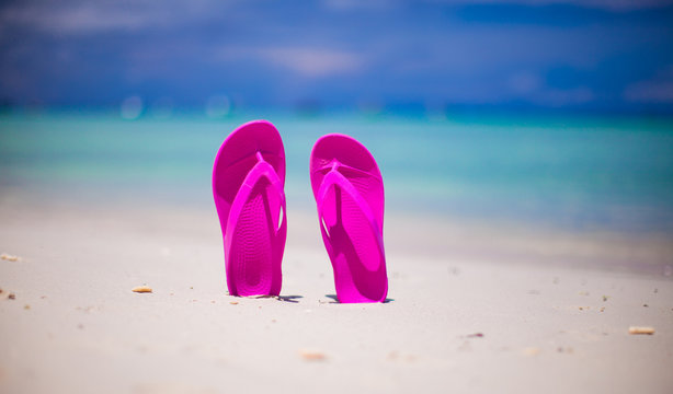 Pink vibrant beach flip flops on white sand on sea background
