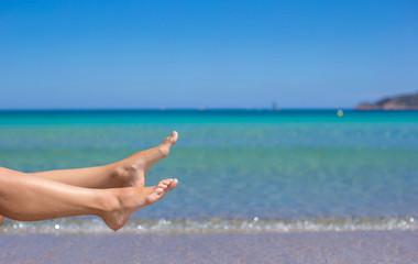 Female tanned slim legs on the white sandy tropical beach