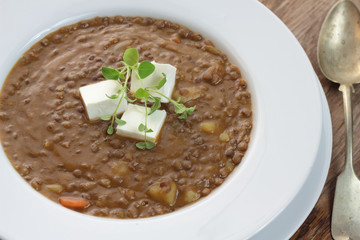 Plate of lentil soup with feta cheese cubes and fresh oregano.