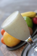 Glass full of banana milk smoothie on a tin plate.