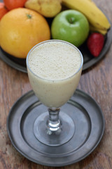 Glass full of banana milk smoothie on a tin plate.