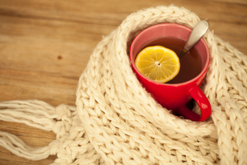 Sickness concept: Cup of hot tea and lemon wrapped with a scarf