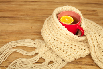 Sickness concept: Cup of hot tea and lemon wrapped with a scarf