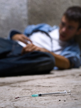 Young drug addict with a syringe in foreground