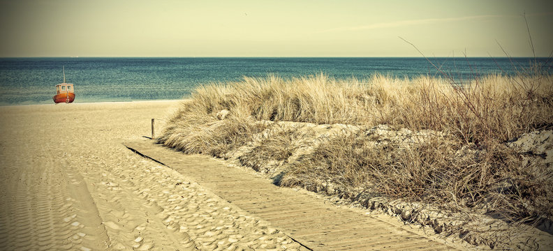 Retro toned panoramic photo of a beach entrance.