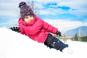 Fototapeta na wymiar Little girl in winter clothes laying in snow waving and smiling
