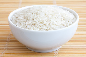 Bowl of uncooked white long grain rice on a bamboo mat.