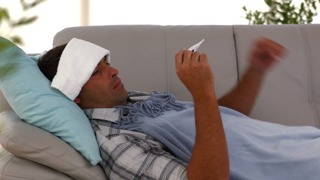 Sick man lying on sofa under a blanket