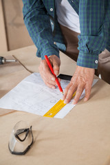 Midsection Of Carpenter Drawing Blueprint At Table