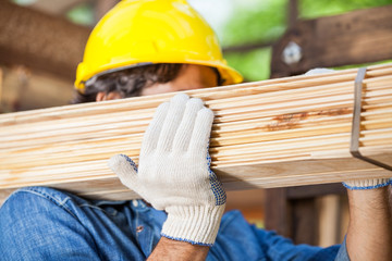 Worker Carrying Tied Wooden Planks At Construction Site