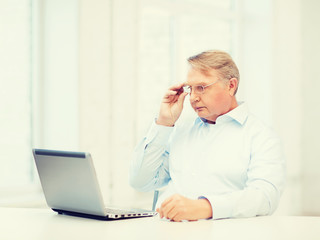 old man in eyeglasses working with laptop at home