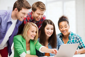 smiling students looking at laptop at school