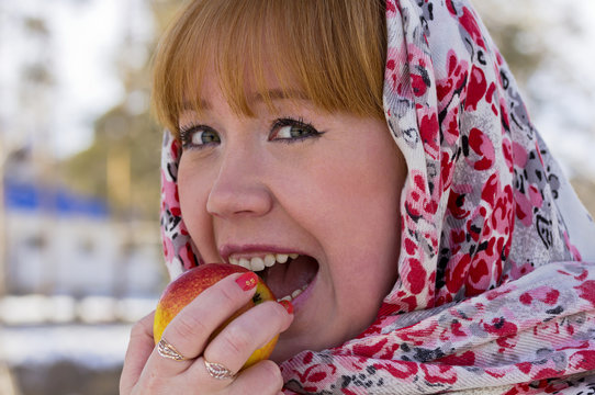Girl in colorful scarf is eating an apple.