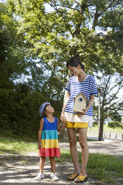 Mother and daughter standing outdoors, holding bird house.