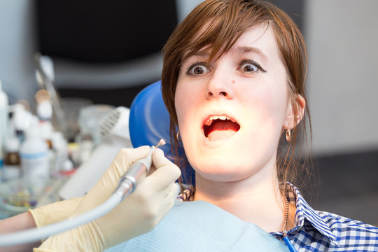 Girl with fear in his eyes looking at drill in hands of dentist