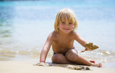 Cute little smiling boy plays on the beach