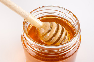 Glass can full of honey and wooden stick in it.