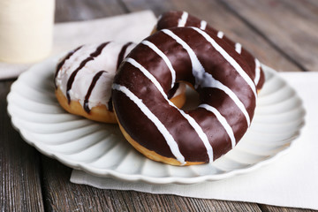 Delicious donuts with icing on plate on wooden background