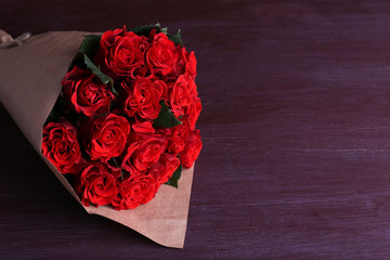 Bouquet of red roses wrapped in paper on wooden background