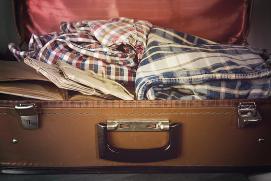 Vintage suitcase open with clothes and books close up