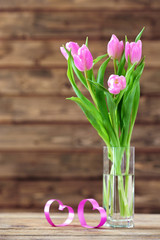 Beautiful pink tulips in vase on table on wooden background