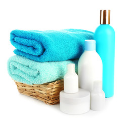 Towels in wicker basket with shampoo bottles isolated on white