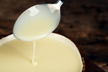 Bowl with condensed milk and spoon on table close up