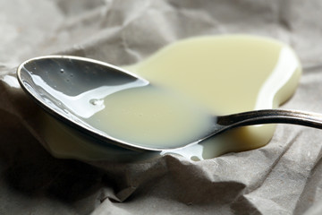 Spoon with condensed milk on paper background