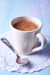 Cup of cocoa with spoon on napkin on wooden background