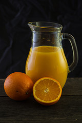 Jug with fresh orange juice, still life art on dark background