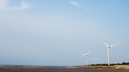 Wind turbines at seaside against blue sky