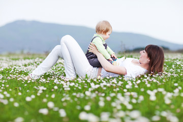Fototapeta premium Happy mother are playing with baby in flowers field