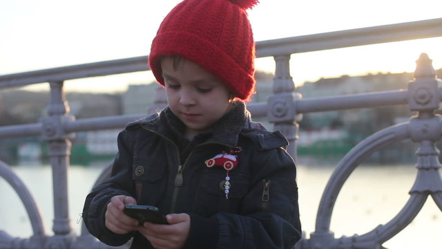 Cute boy, playing with phone on sunset, outdoor